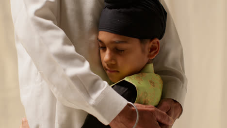 Nahaufnahme-Studioaufnahme-Eines-Jungen-Sikh-Jungen-Mit-Turban-Und-Haarknoten,-Der-Seinen-Großvater-Vor-Einfarbigem-Hintergrund-Umarmt-3